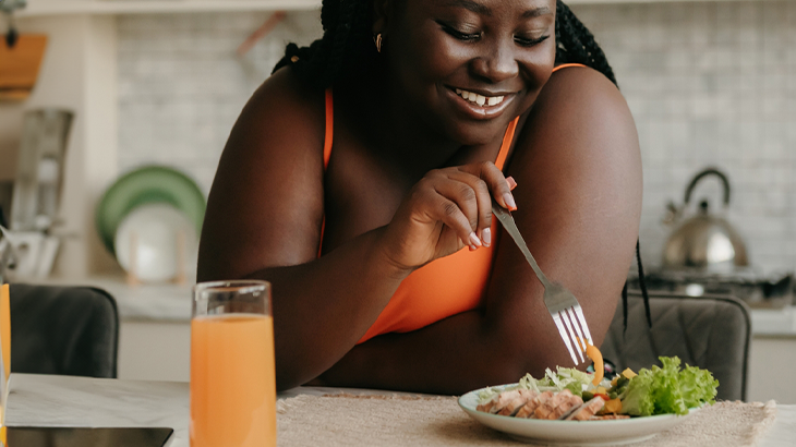 Mulher na frente de um prato com comida espetando o garfo no alimento